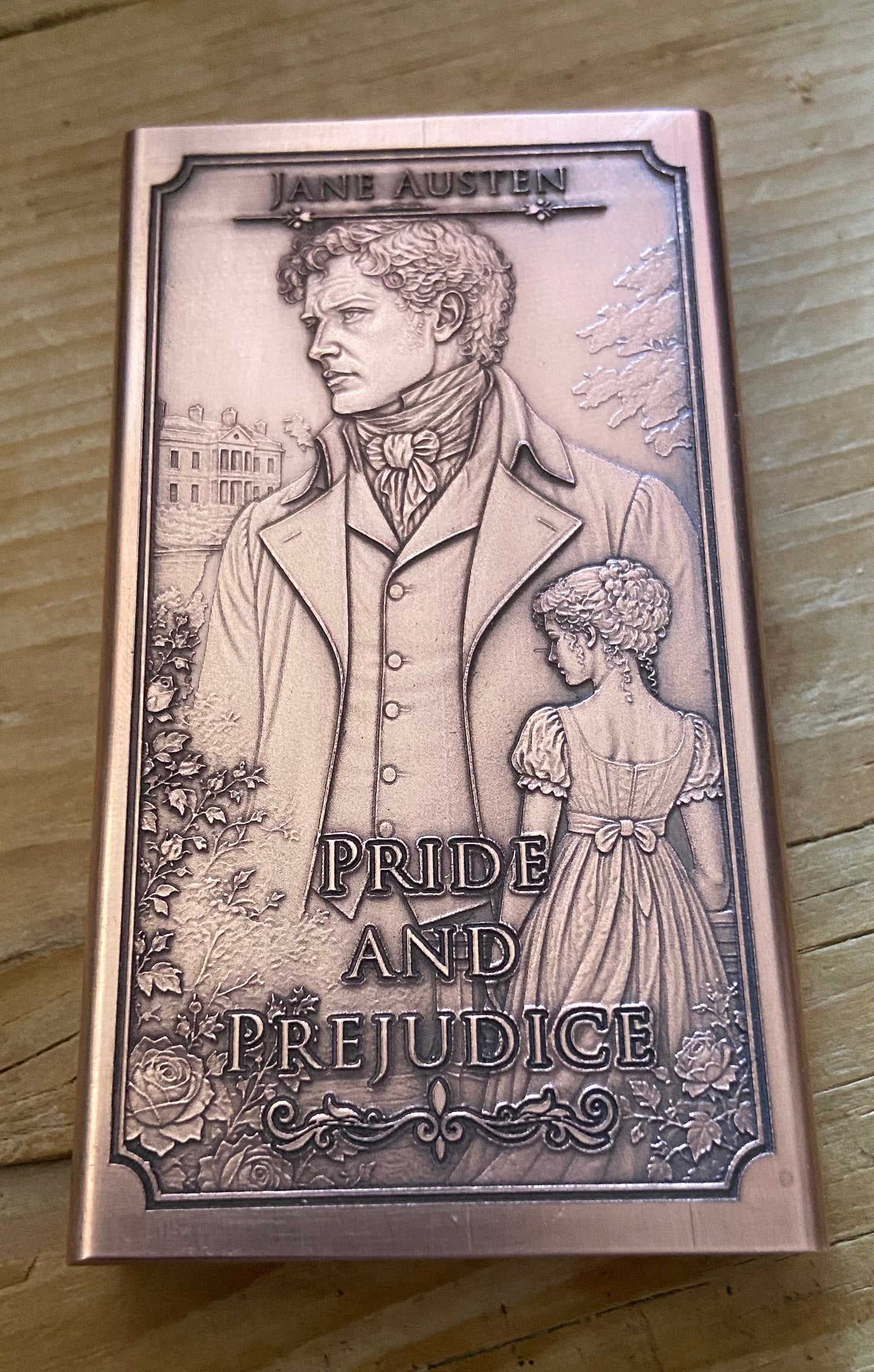 A rectangular book or box cover for Jane Austen's Pride and Prejudice, featuring an embossed sepia-toned illustration of a man and a girl with the title text, placed on a wooden surface.