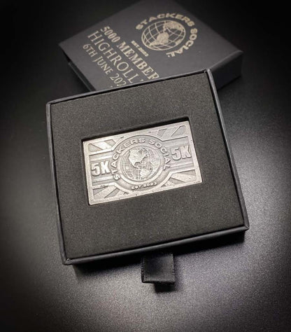 A 999 fine silver Stackers Social 5K displayed inside an open black presentation box, with the matching closed box and an engraved note behind it on a dark surface.