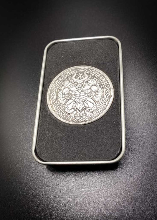 A silver-toned circular metal medallion featuring a winged demon or gargoyle figure, displayed inside a black rectangular case with a silver border on a dark background.